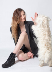 White young european woman with a dog sitting in black on the floor isolated on light grey