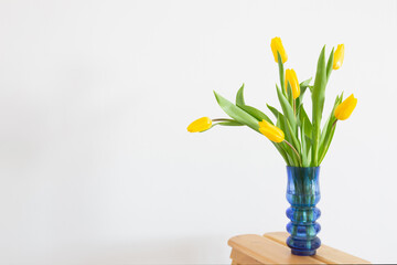 yellow tulips in blue glass vase on white background