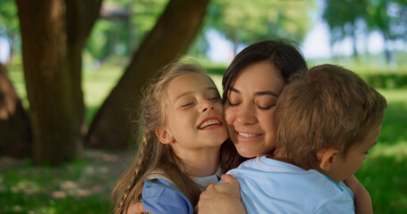 Children hugging happy mother close up. Lovely family picnic in park meadow.