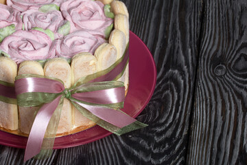 Cake with Savoiardi cookies and marshmallow roses. Tied with ribbon. The ribbon is tied into a bow.