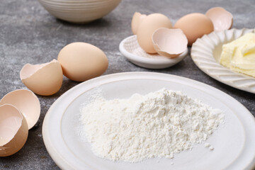 Baking ingredients: Butter, flour in plates,  broken eggs on the table. Shallow depth of field