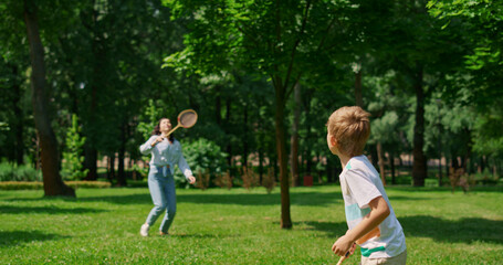 Active boy playing badminton with mother back view. Sport in family life concept