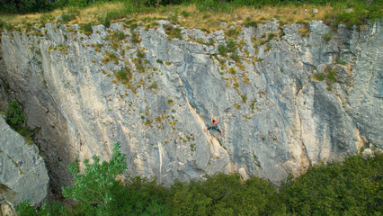 AERIAL: Flying above a woman rock climbing up a rocky cliff in rural Slovenia.