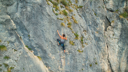AERIAL: Drone view of a female rock climber ascending up a challenging cliff.