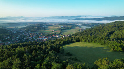 Fototapeta na wymiar AERIAL: Mist covering the valley in Slovenian countryside clears up at sunrise.
