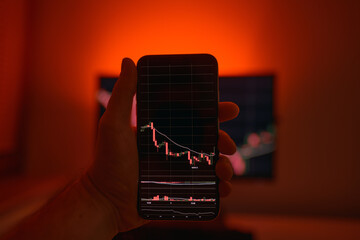 Mobile phone and computer screen show cryptocurrency graph. Trading online. Concept of bitcoin exchange rate going down with red background