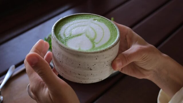 Human hands holding hot green matcha latte cup, healthy dietary lunch with trendy vegan avocado toast 