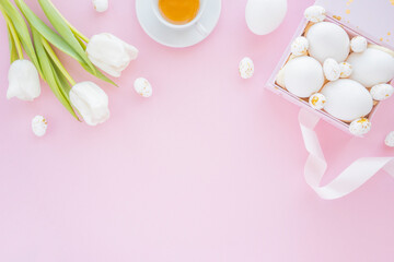 Fototapeta na wymiar Top view of colorful eggs in a box with tulips, cup of tea for spring holiday easter. Flat lay, pink background