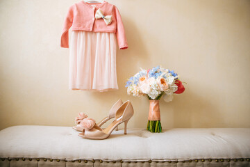 Wedding bouquet on sofa near bridal shoes and flower girl dress