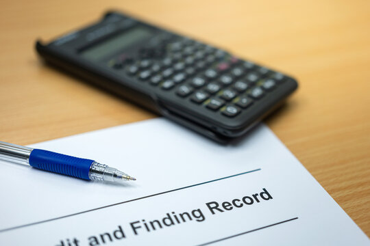 A ball pen is placed record document paper with blurred background of calculator on wooden table. Business and finance workplace scene photo. Close-up and selective focus at pen nib.