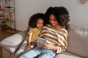 Two beautiful black girls of different age playing a game on the electronic device at home. Loving...