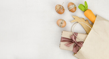 Obraz na płótnie Canvas Eggs, carrots and a wooden hare in a kraft bag.on a light wide background.Minimalistic decor for Easter. Spring Religious holiday.The concept of a holiday and shopping for Easter.