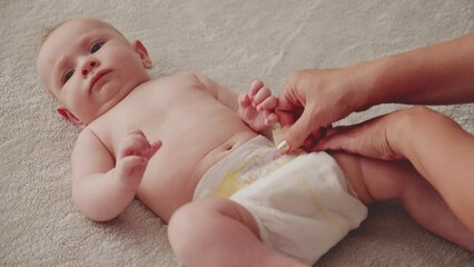Mother changing diaper on her newborn baby. Mother changing diaper on her newborn baby indoors. The child moves his legs.  Dry skin.  Mom puts diapers on her newborn baby on a changing table.