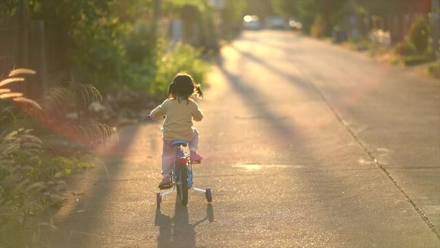 Backside of Asian toddler girl child learning to ride bicycle in sunny summer day, kid cycling at park, baby sport concept