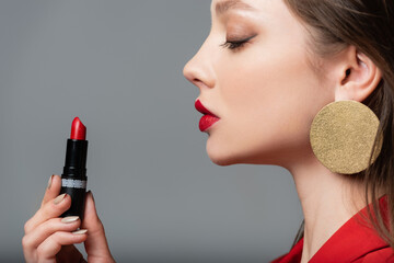 side view of young model holding red lipstick isolated on grey.