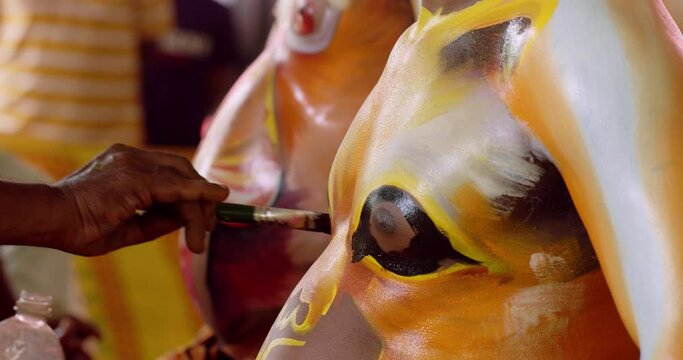 Indian dance performer getting a tiger painting on his body as part of Pulikali - Tiger dance festival in Kerala, India. Close up, camera tilts down from chest to stomach.