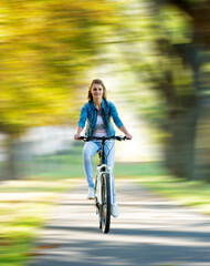 young slender blonde woman in jeans rides a bike in a summer park