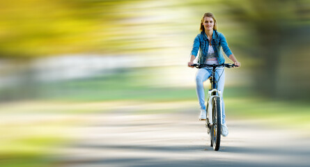 young slender blonde woman in jeans rides a bike in a summer park