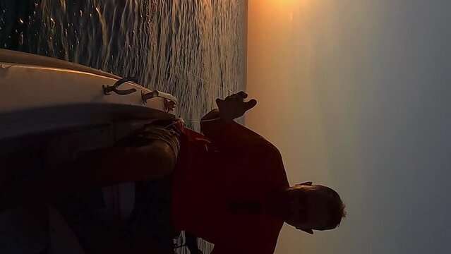 Silhouette of fisherman at sunset trolling fishing with hand and line while boat is moving. Slow-motion VERTICAL format