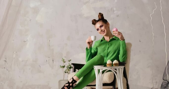 Fashionable photo shoot of young girl with coffee and cake in modern studio. Girl in green outfit in cafe poses for photo and video.