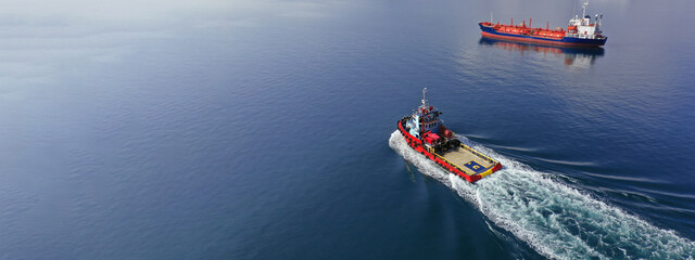 Aerial drone ultra wide photo of industrial tug assisting vessel cruising near container terminal...