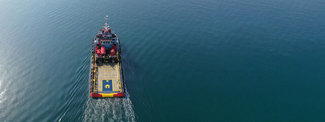 Aerial drone ultra wide photo of industrial tug assisting vessel cruising near container terminal...