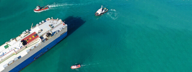 Aerial drone ultra wide photo of large car carrier ro ro vessel guided by tug boats to depart from...