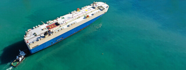Aerial drone ultra wide photo of large car carrier ro ro vessel guided by tug boats to depart from...