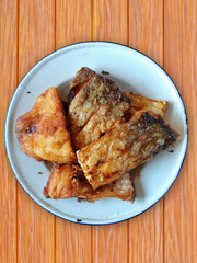 Brown fried fish in white plate on brown wooden background. Concept fried and high-fat food.