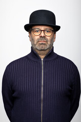 Portrait middle aged man with glasses, bowler hat and round glasses. He is wearing a dark jumper