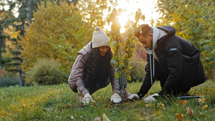 Young happy hispanic couple in love in park planting tree in gloves fertilize soil take care natural plants environment world ecology reforestation symbol relationship beginning family life hobby © Yuliia