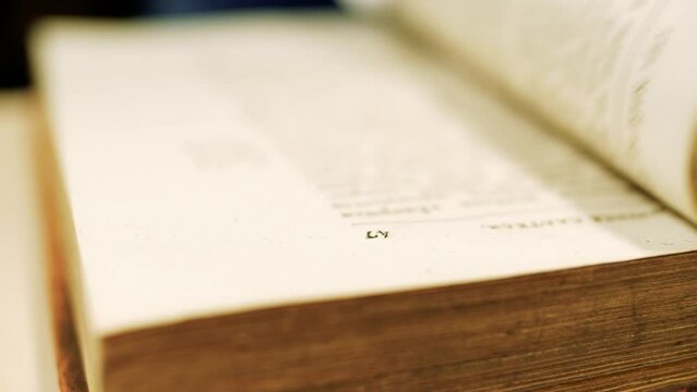 Someone is slowly leafing through an old book on the table. Page numbers are visible