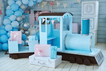 A room decorated for a children's holiday. A toy locomotive, balloons and boxes with gifts. Blue and pink colors.