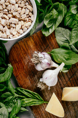 Photo of a fresh healthy ingridients like green basil, fresh garlic, roast nut, parmegiano cheese to make homemade pesto sauce on a wooden desk indoors daylight
