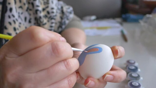 woman paints an Easter egg with paints. Easter bunny drawing on a white egg