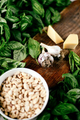 Photo of a fresh healthy ingridients like green basil, fresh garlic, roast nut, parmegiano cheese to make homemade pesto sauce on a wooden desk indoors daylight