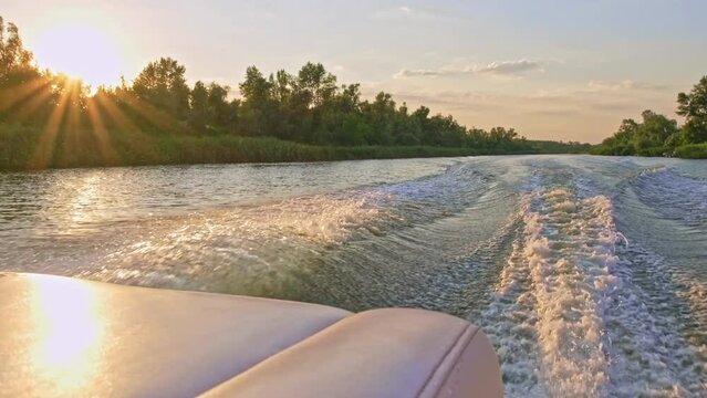Slow-motion clip: The motorboat creates beautiful waves, splashes from the running motors moving at high speed. View from the stern of the boat on a beautiful summer sunset. Engine churns the water