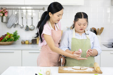 mother support down syndrome teenage girl or her daughter using a mold made of rolled dough on kitchen table