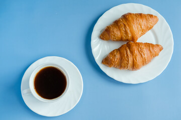 Croissants and morning coffee in a white cup on a blue background, top view