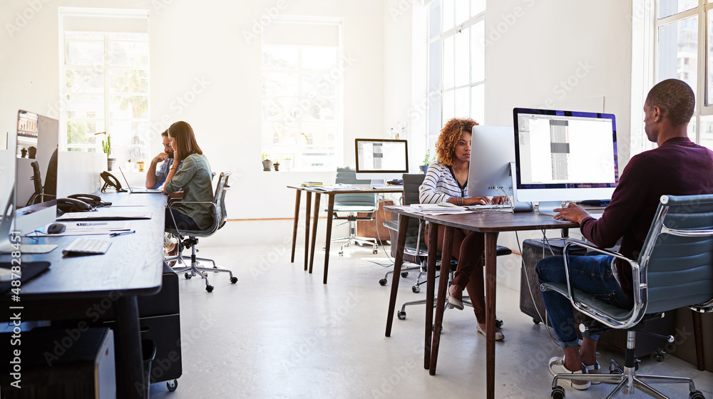 Poster Working in an open plan office. Shot of colleagues working on their computers in an open plan office.