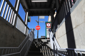 a stop sign at the top of a staircase with a gray metal hand rail on a black pole with two street...