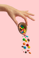 Female hand holds chocolate Easter egg from which colorful sweets pour out. Pastel pink background.