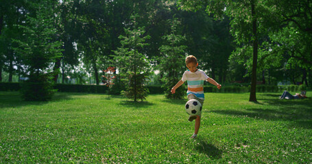 Fototapeta premium Little boy kicking soccer ball. Focused child practicing in summer park alone.