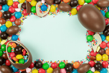 Fototapeta na wymiar Frame of chocolate Easter eggs and colorful sweets on light blue background. Space for text.
