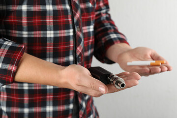 Man with cigarettes and vaping device on light background, closeup. Smoking alternative