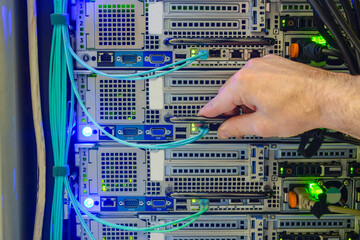 Service work in the datacenter server room. The hand of a technician with a communication Internet wire is a close-up. Connection of trunk cables to the network interface of the modern server