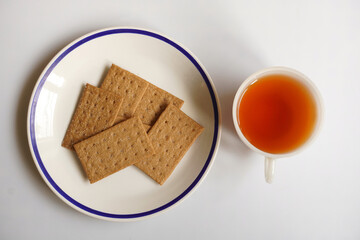 Flat lay view of crispy sugar-coated crackers and a cup of black tea, lit by window lighting, on white background.