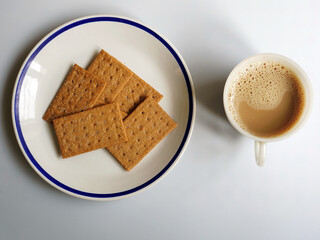 Flat lay view of coffee biscuits and a cup of milked coffee, lit by window lighting, on white background