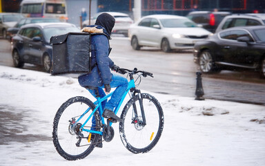 Food delivery man on bike hard work at winter day. Delivery man with backpack bikes through blizzard to deliver online food orders. Restaurants delivery service. Takeaway courier on the road by bike