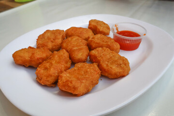 Crispy chicken cakes placed on a white plate and orange chili sauce.